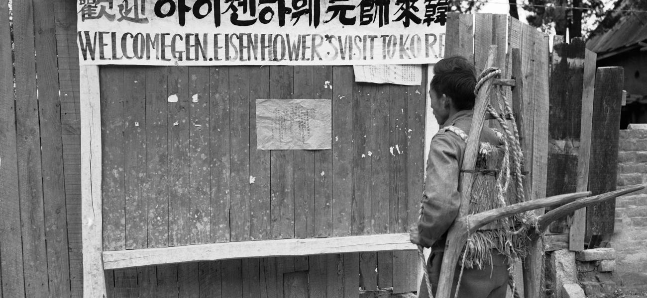 A Korean, with an “A” frame carrier strapped to his back, pauses on a Seoul, Korea, street on Nov. 28, 1952 to read sign posted in English and Korean in anticipation of a visit by President-elect Dwight D. Eisenhower, Nov. 27, 1952. (AP Photo/George Sweers)