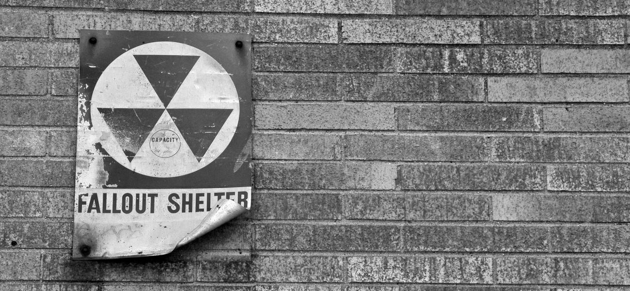 Black and white fallout shelter sign on brick wall.