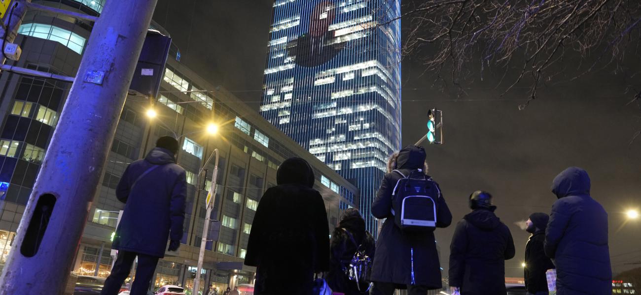 People look up at an image of Russian President Vladimir Putin, projected on the facade of a business building, in St. Petersburg, Russia, Dec. 18, 2024, announcing Putin's annual news conference and call-in show. (AP Photo/Dmitri Lovetsky)