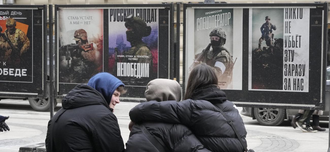 Young people sit near a street exhibition of military posters named 'Together to Victory' dedicated to Russian army in St. Petersburg, Russia, Monday, Feb. 24, 2025. (AP Photo/Dmitri Lovetsky)
