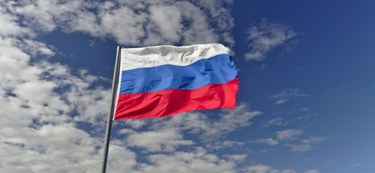 Russian flag, a little raggedy, against backdrop of blue sky and clouds.